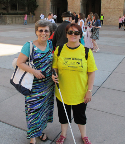 Photo shows Dona standing with a woman wearing a yellow shirt and carrying a white cane, both are smiling at the camera.